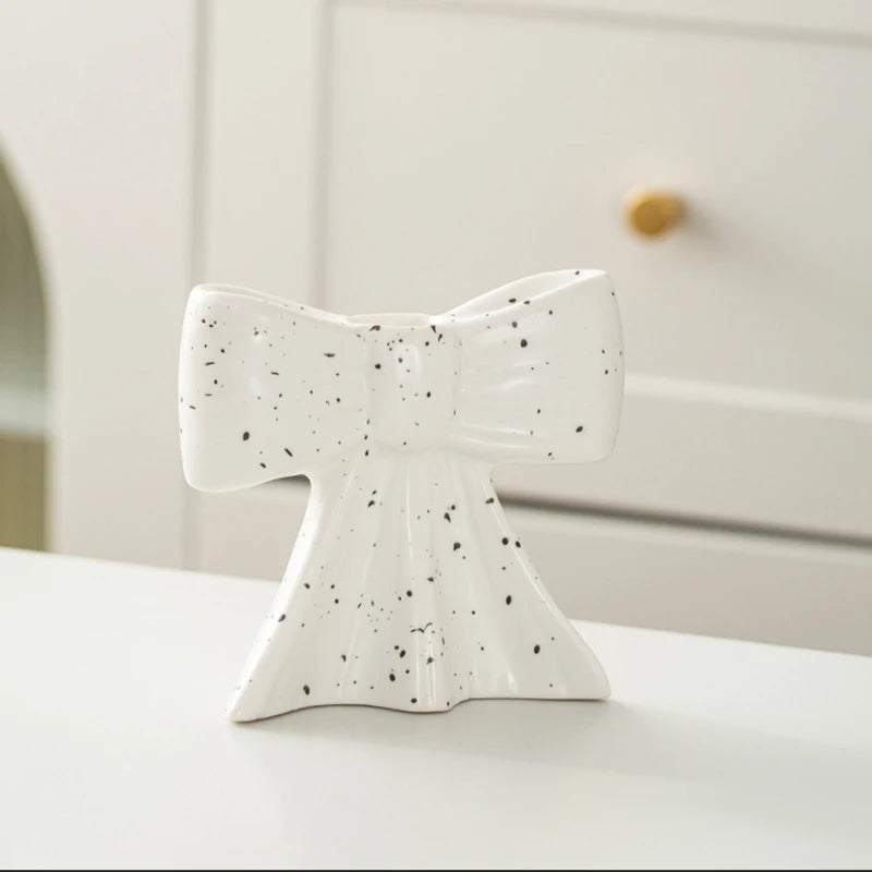 A white ceramic bow candle holder with black speckles sits on a white surface.
