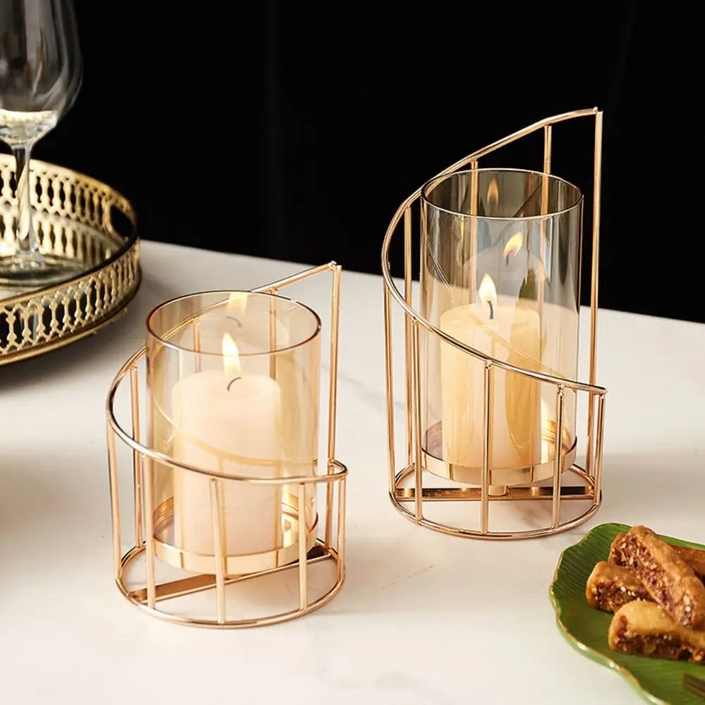 Elegant gold metal candle holder with glass cylinder and flame on a white surface.