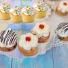 A 3-tier rainbow cupcake stand displaying various frosted cupcakes and cookies on a light blue wooden surface.