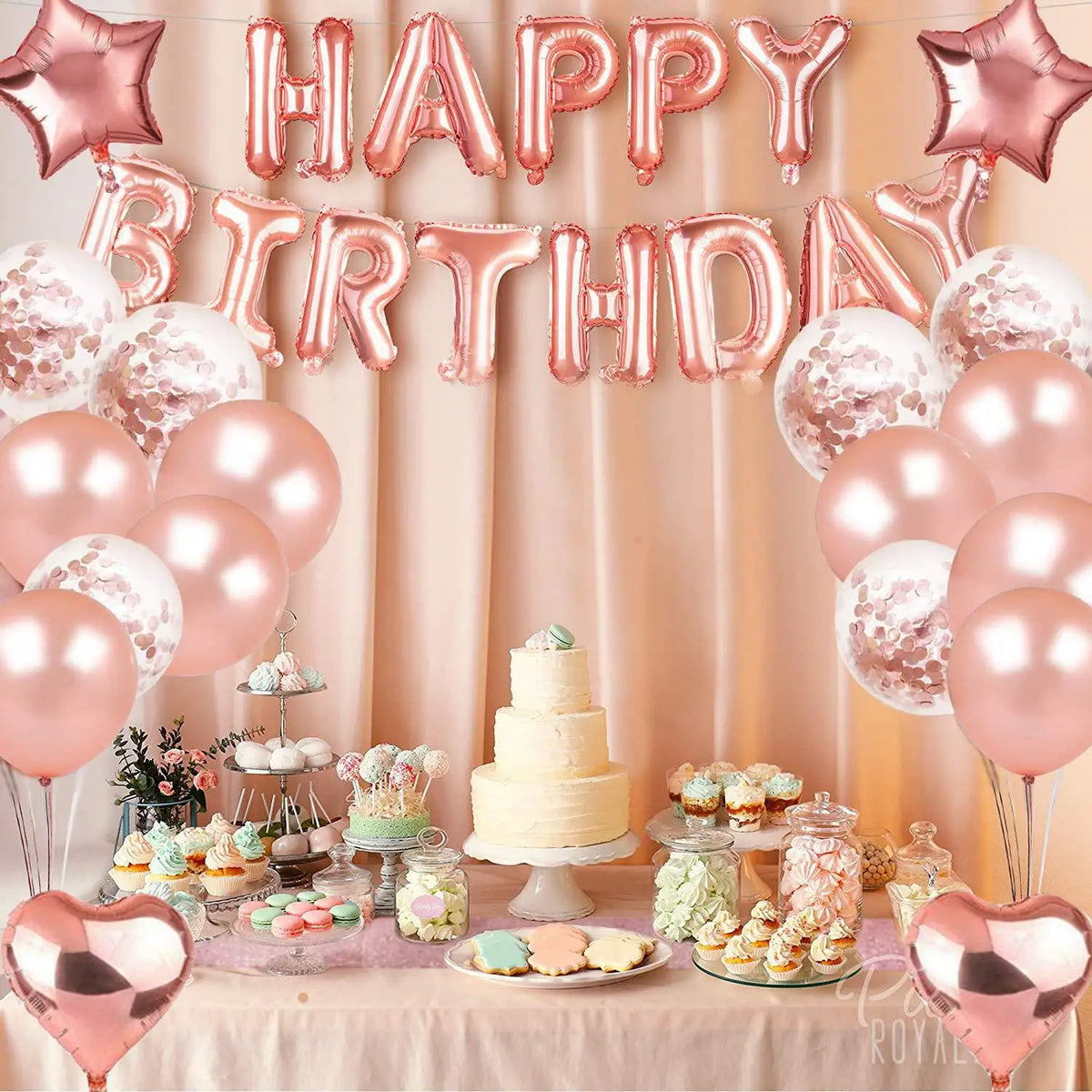 A pink and rose gold balloon decoration set featuring letters, balloons, and a tiered cake for a birthday celebration.