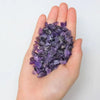 A hand holds a pile of purple amethyst gemstone chips for crafts and jewelry making.