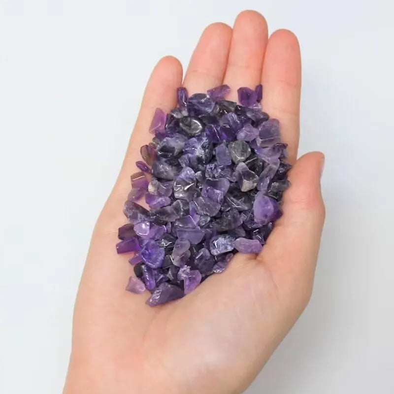 A hand holds a pile of purple amethyst gemstone chips for crafts and jewelry making.