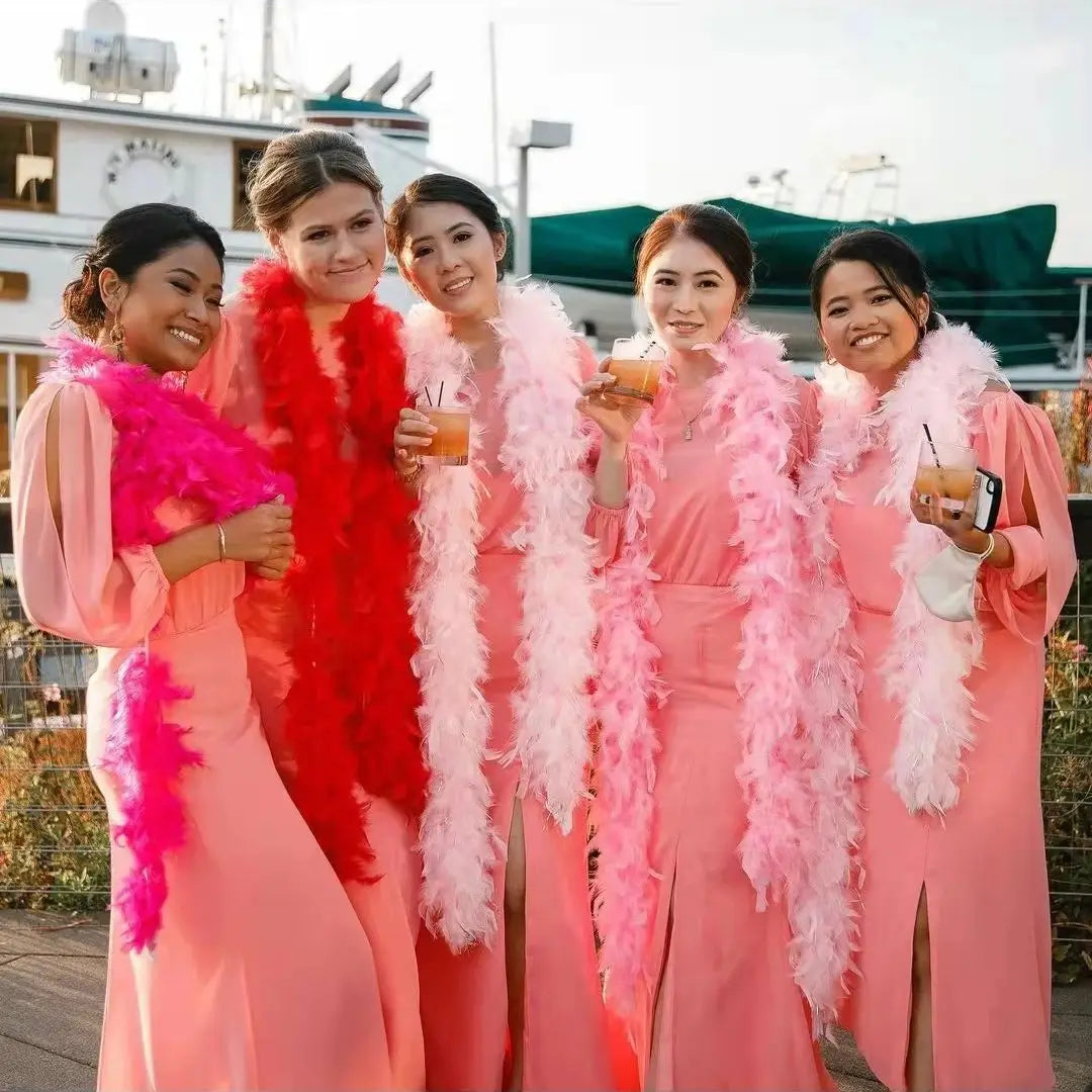 Five women wearing pink dresses and natural turkey feather boas posing outdoors.