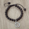A black beaded bracelet with a silver zodiac charm is displayed on a wooden surface.