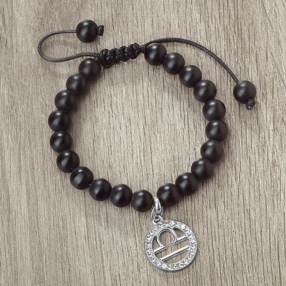 A black beaded bracelet with a silver zodiac charm is displayed on a wooden surface.