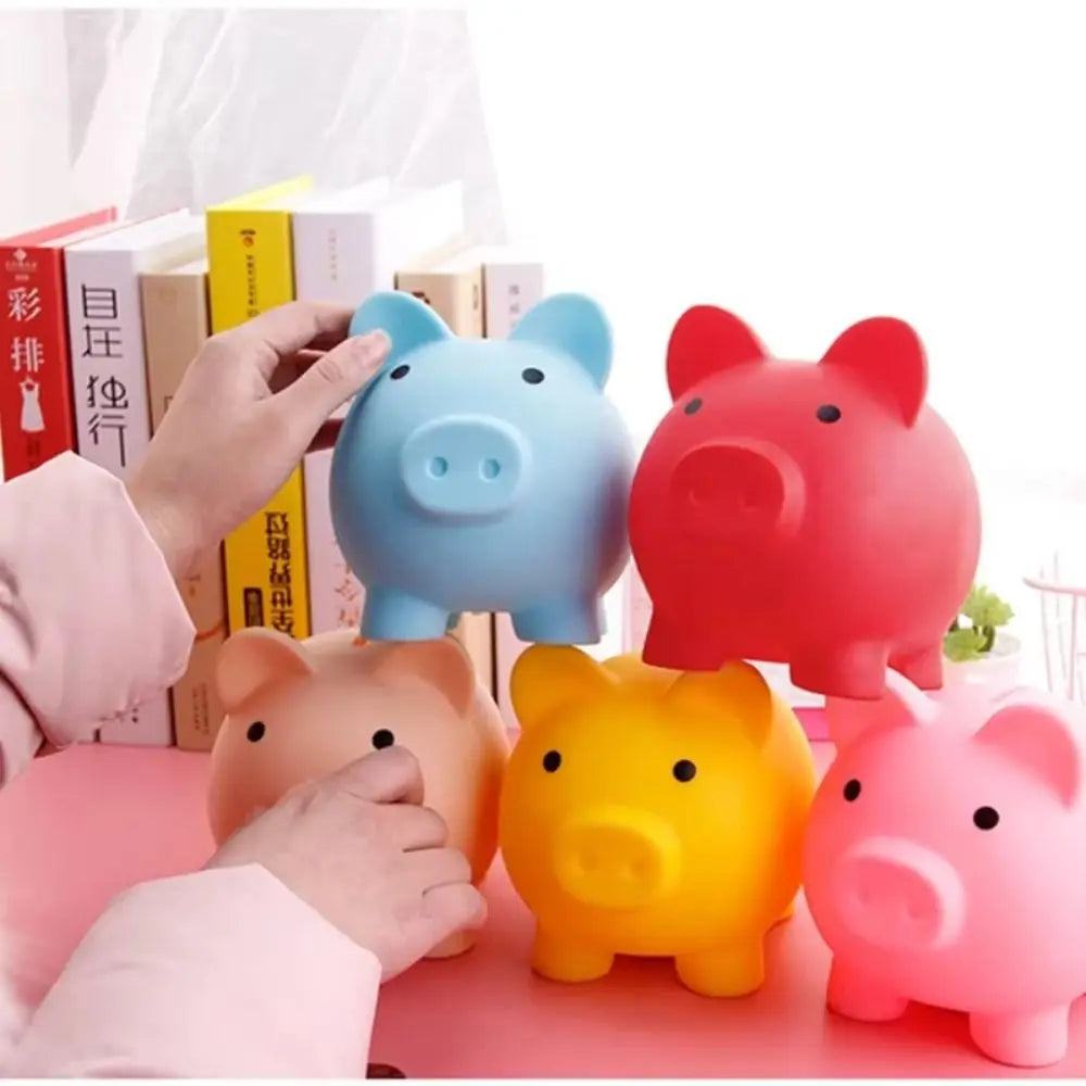 A collection of colorful pig-shaped coin storage banks in blue, red, and yellow are displayed on a pink surface.