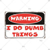 A vintage metal warning sign with a black background and red text that reads WARNING I DO DUMB THINGS.