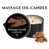 A black jar of massage candle with a lit wick and pieces of agarwood wood visible nearby.