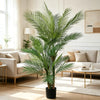 An artificial triple trunk palm tree in a black pot standing in a bright, modern living room.