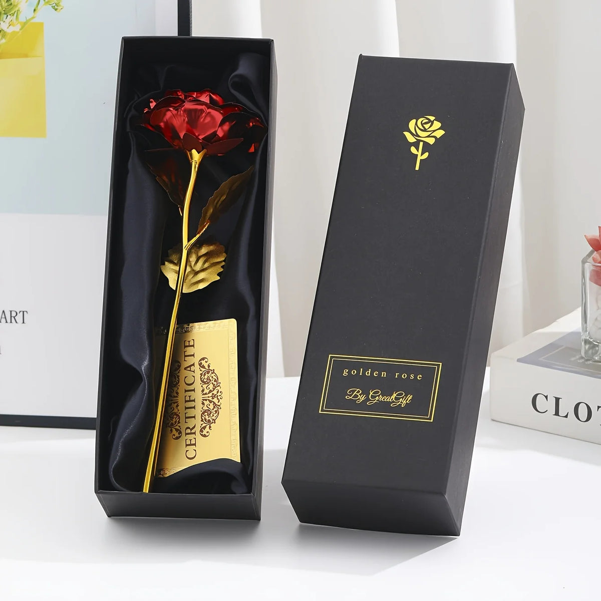 A black gift box displaying a gold foil rose flower and a card, set against a white background.