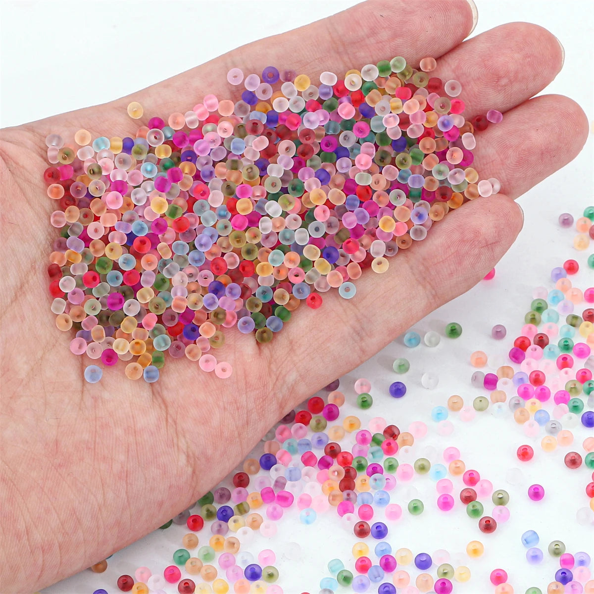 A hand holds a pile of multi-colored frosted glass rice beads for jewelry making.