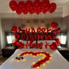 A bed decorated with red foil birthday balloons and a heart-shaped flower arrangement on the white bedding.