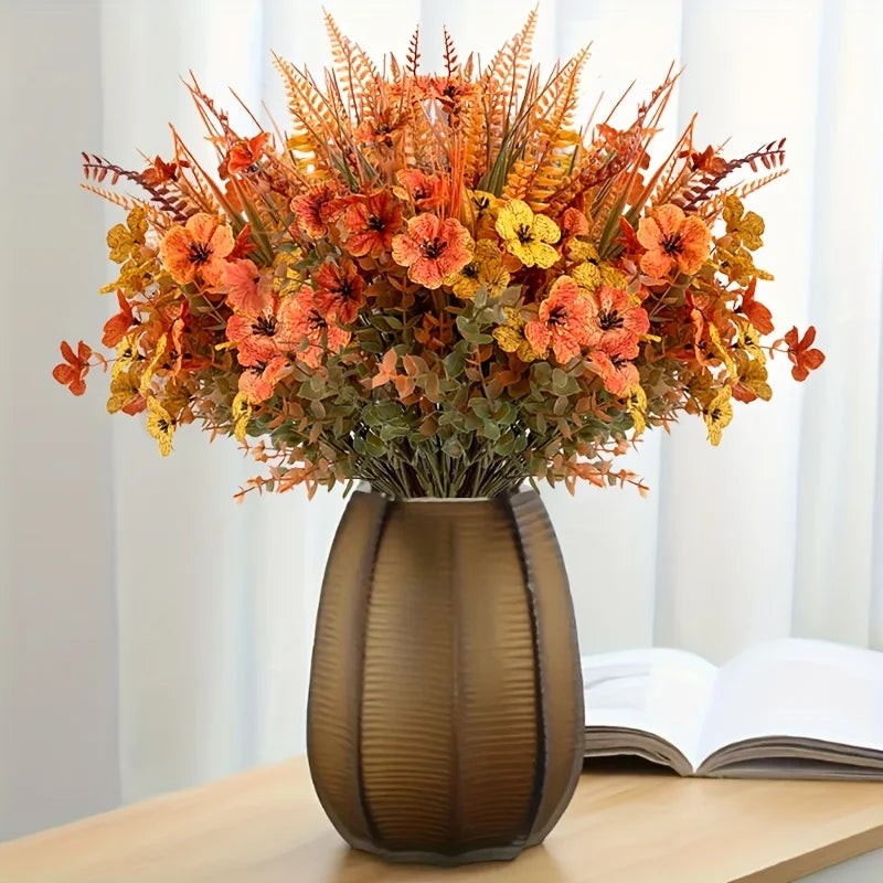 A bouquet of artificial autumn floral decorations featuring orange, yellow, and rust-colored foliage in a dark vase.