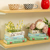 Vase en céramique à trois couches en forme de livre avec des arrangements floraux sur une étagère en bois.