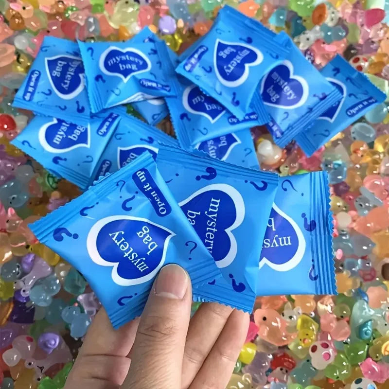 A hand holds a blue packet of glow in the dark resin decor for fairy gardens amidst colorful glitter.