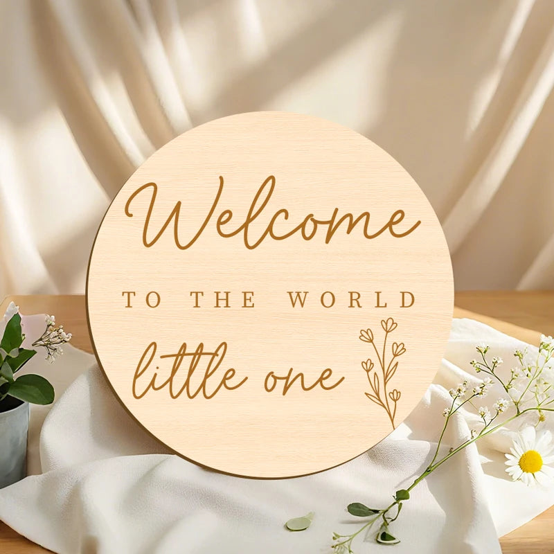 A round wooden welcome sign with the text Welcome to the world little one on a white cloth.