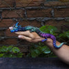A hand holds a vibrant, color-changing flexible dragon figurine against a dark, textured background.
