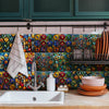 A kitchen backsplash featuring colorful mosaic tiles, a white sink, and dark green cabinetry.