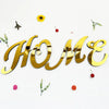 Gold 3D acrylic letter wall stickers spelling HOME with small decorative leaves and berries