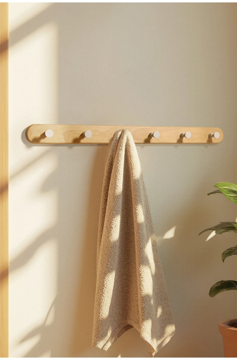 A beige towel is hanging on a light wood wall hook rack with four visible hooks.