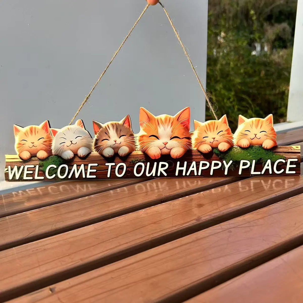 A wooden sign featuring several orange and cream-colored cat faces, hanging by twine on a wooden plank.