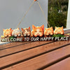 A wooden sign featuring several orange and cream-colored cat faces, hanging against a light gray wall.