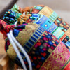 A close-up of a colorful, patterned fabric drawstring gift pouch with white cord and decorative stitching.
