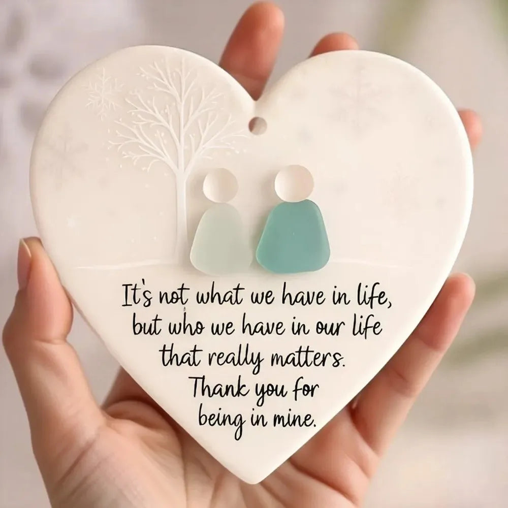 A white heart-shaped acrylic pendant featuring a tree design and two silhouette figures, with text about relationships.