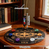 Un long collier or avec un pendentif noir et des cristaux colorés, exposé au-dessus d'un jeu de divination en bois.