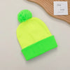 A bright neon yellow knitted beanie with a fluffy green pom-pom and a contrasting lime green cuff.