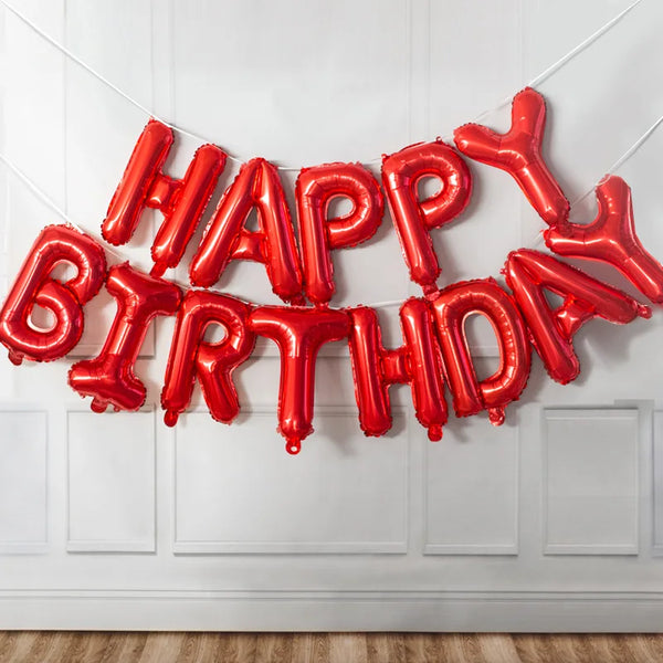 A red foil balloon banner spelling out Happy Birthday strung across a white door.
