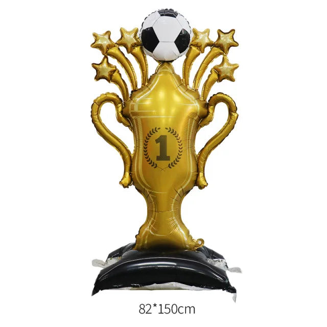 A golden foil trophy balloon shaped like a soccer trophy with a black base and a white soccer ball on top.