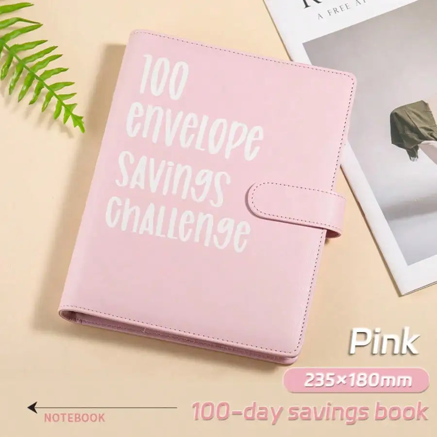 Pink envelope savings challenge notebook with a leather cover and a green leaf in the background