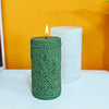 A green silicone candle mold shaped like a laurel wreath with a flame on top, next to a white pillar candle.
