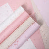 Rolls of pink and white decorative packaging paper with dried flower petals on a light background