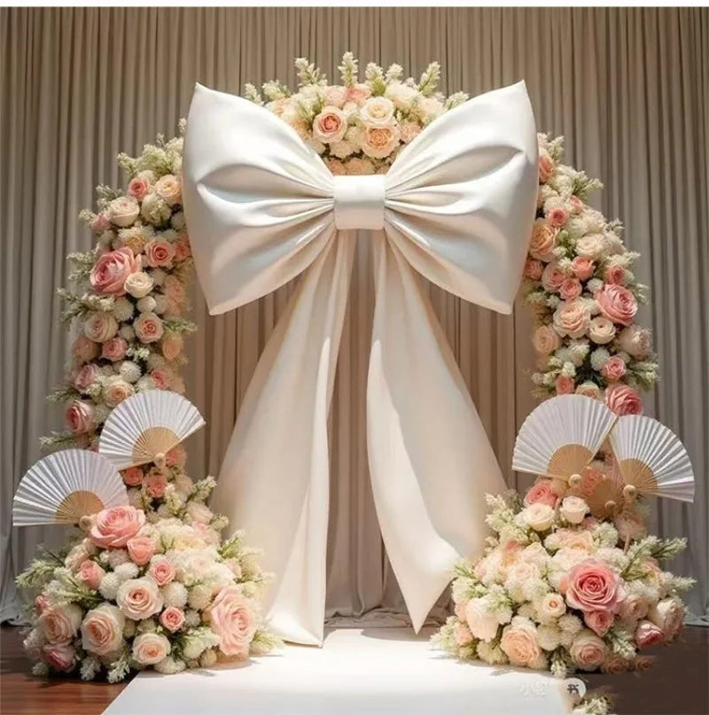 Giant satin bow with long tulle drape used as event decor featuring pink and cream floral arrangements
