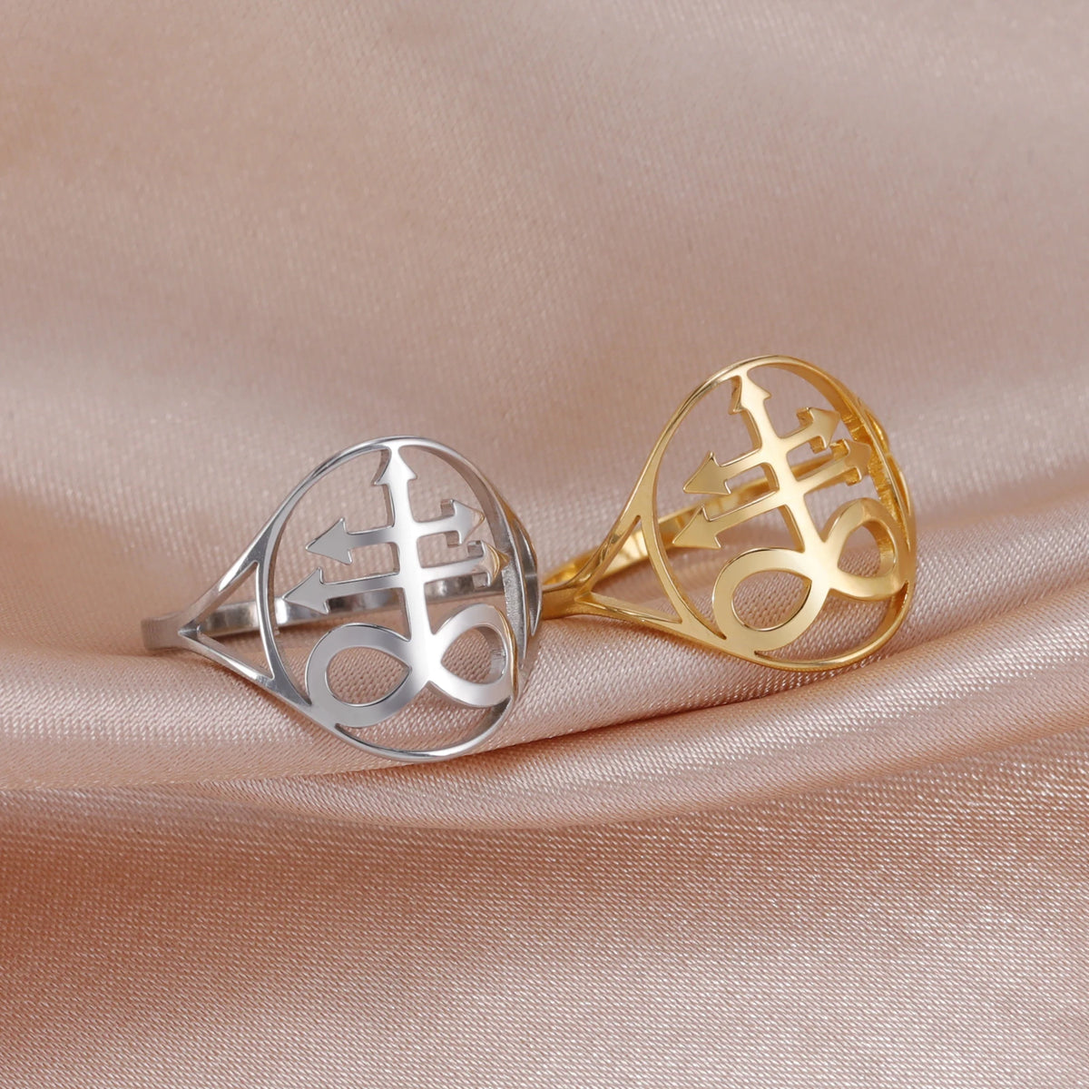Silver and gold signet rings featuring a leviathan cross design displayed on a soft pink fabric.
