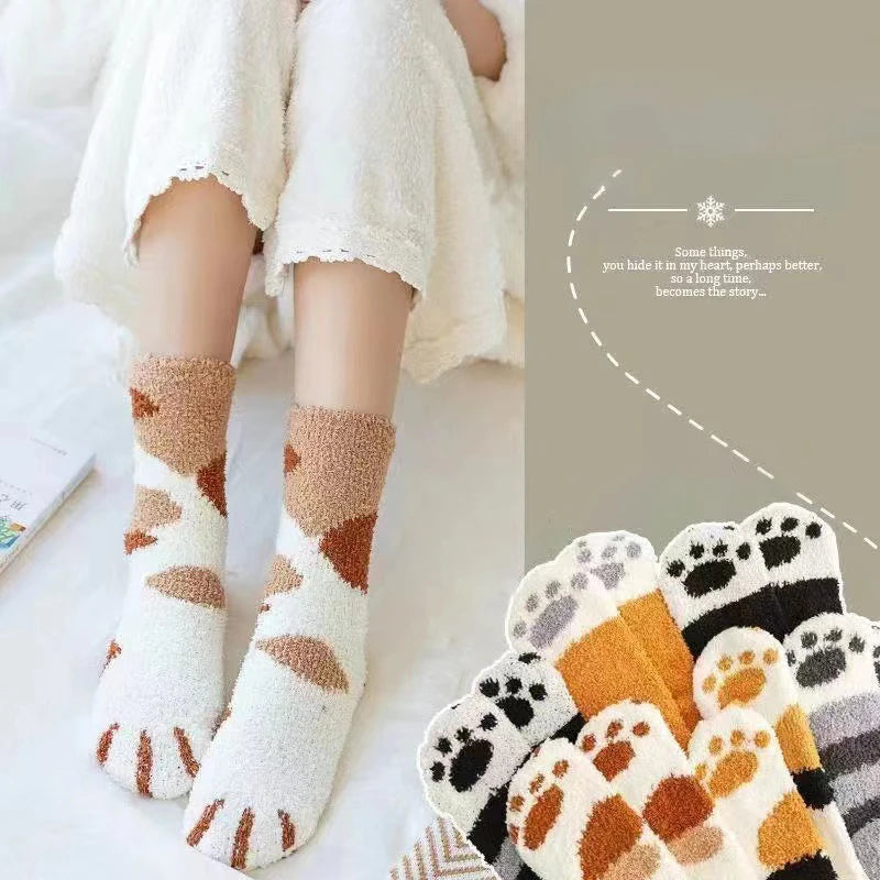 A pair of white plush socks with brown cat paw prints are shown on a person's feet, set against a soft background.