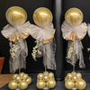 Three gold balloons displayed on an adjustable metal column stand against a dark background.