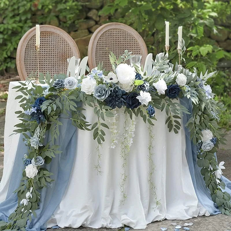 A floral arrangement featuring white and blue roses and eucalyptus greenery displayed on a white draped table.