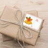 A brown gift wrapped with twine and featuring a yellow bell sticker with a red bow and the text Merry Christmas