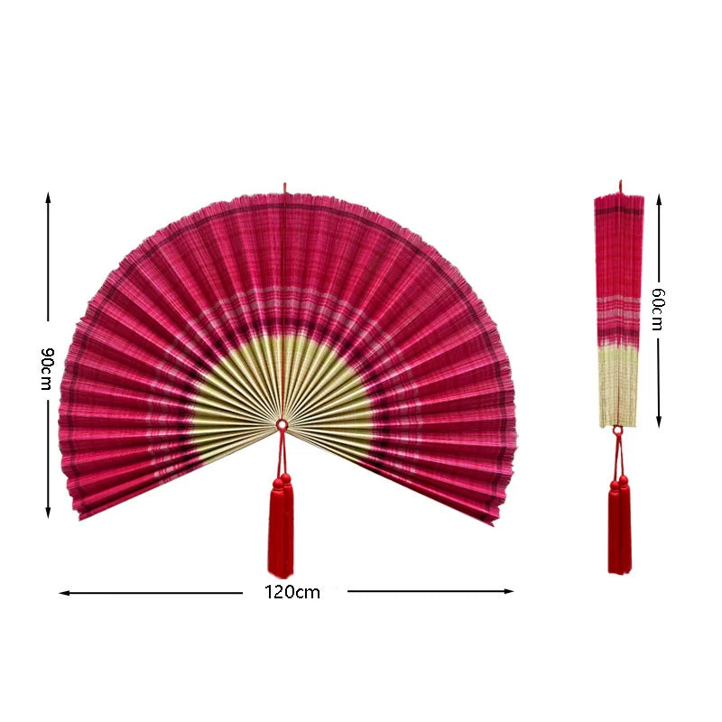 Handwoven bamboo wall fan decor in pink and green with a tassel hanging from the bottom.
