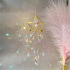 A golden crystal hanging suncatcher decoration with dangling clear and purple crystals against a soft, light background.