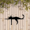 A black silhouette of a cat sculpture is mounted on a light wood panel with green foliage above.