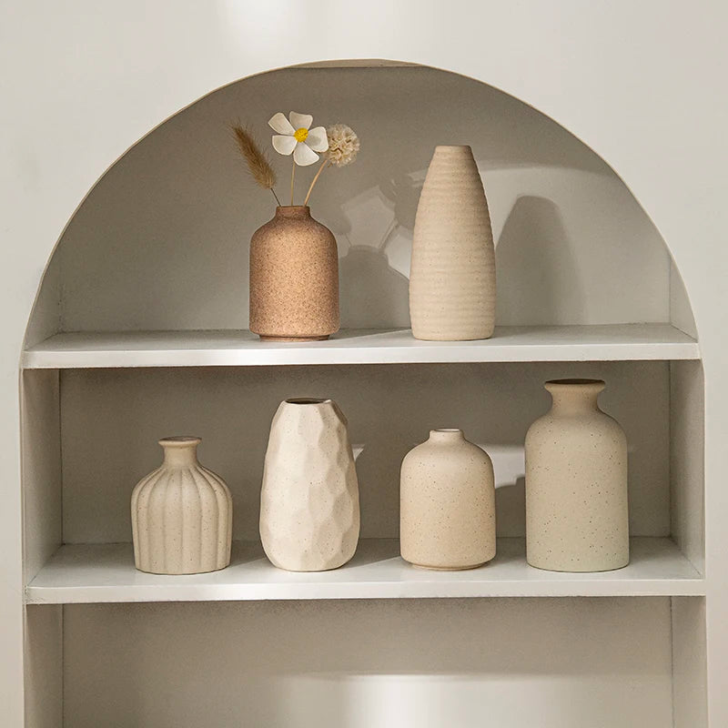A display of minimalist ceramic vases and a dried flower in an arched shelf setting.
