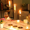 A set of three gold metal taper candle holders with lit candles displayed on a white table.