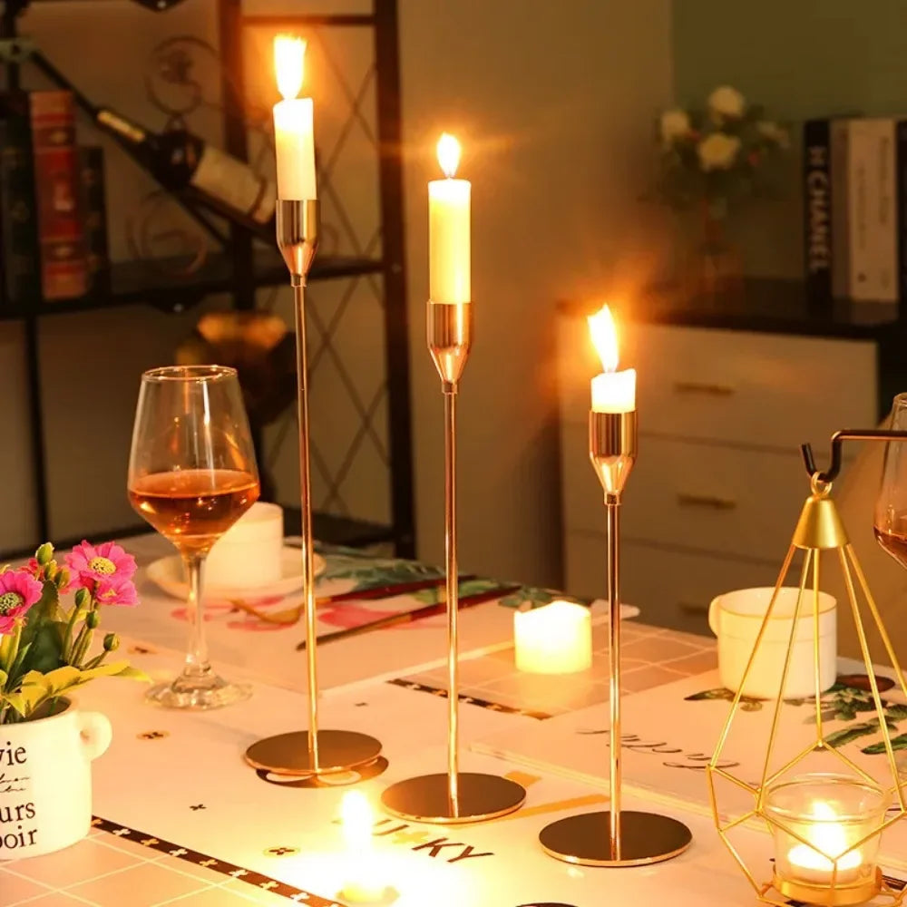 A set of three gold metal taper candle holders with lit candles displayed on a white table.