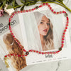 A red rosary necklace with amber beads and a gold charm displayed on a white background.