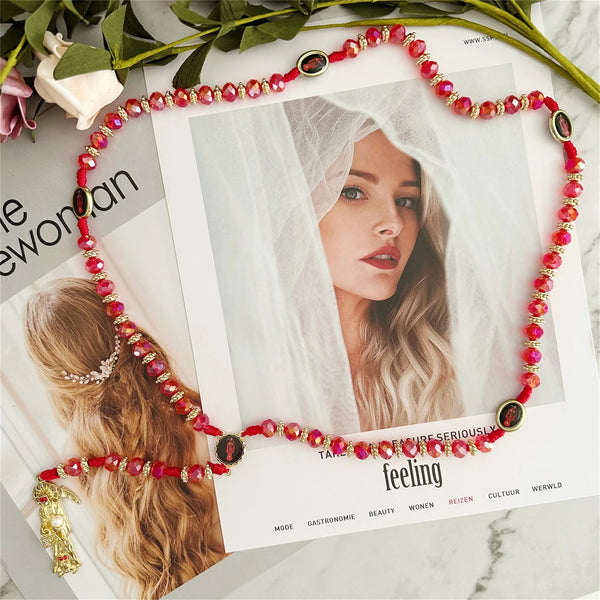 A red rosary necklace with amber beads and a gold charm displayed on a white background.