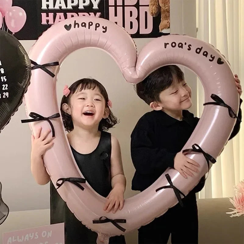 Two children holding a large pink heart-shaped balloon decoration for a birthday celebration.